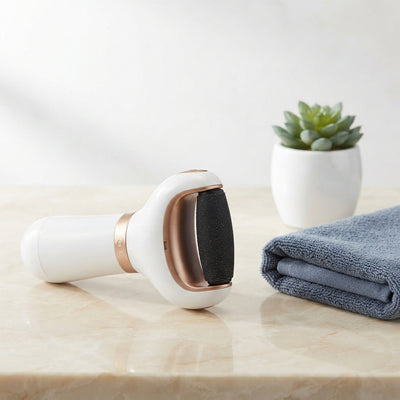 Electric callus remover tool sitting on a cream marble countertop next to a slate blue towel.